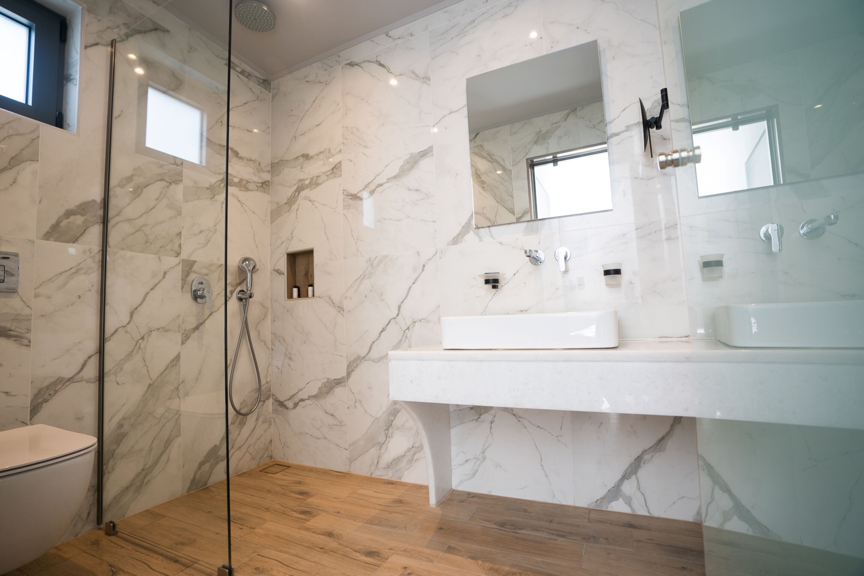 A modern bathroom with a glass-enclosed shower, a white sink, and marble walls.