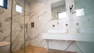 A modern bathroom with a glass-enclosed shower, a white sink, and marble walls.