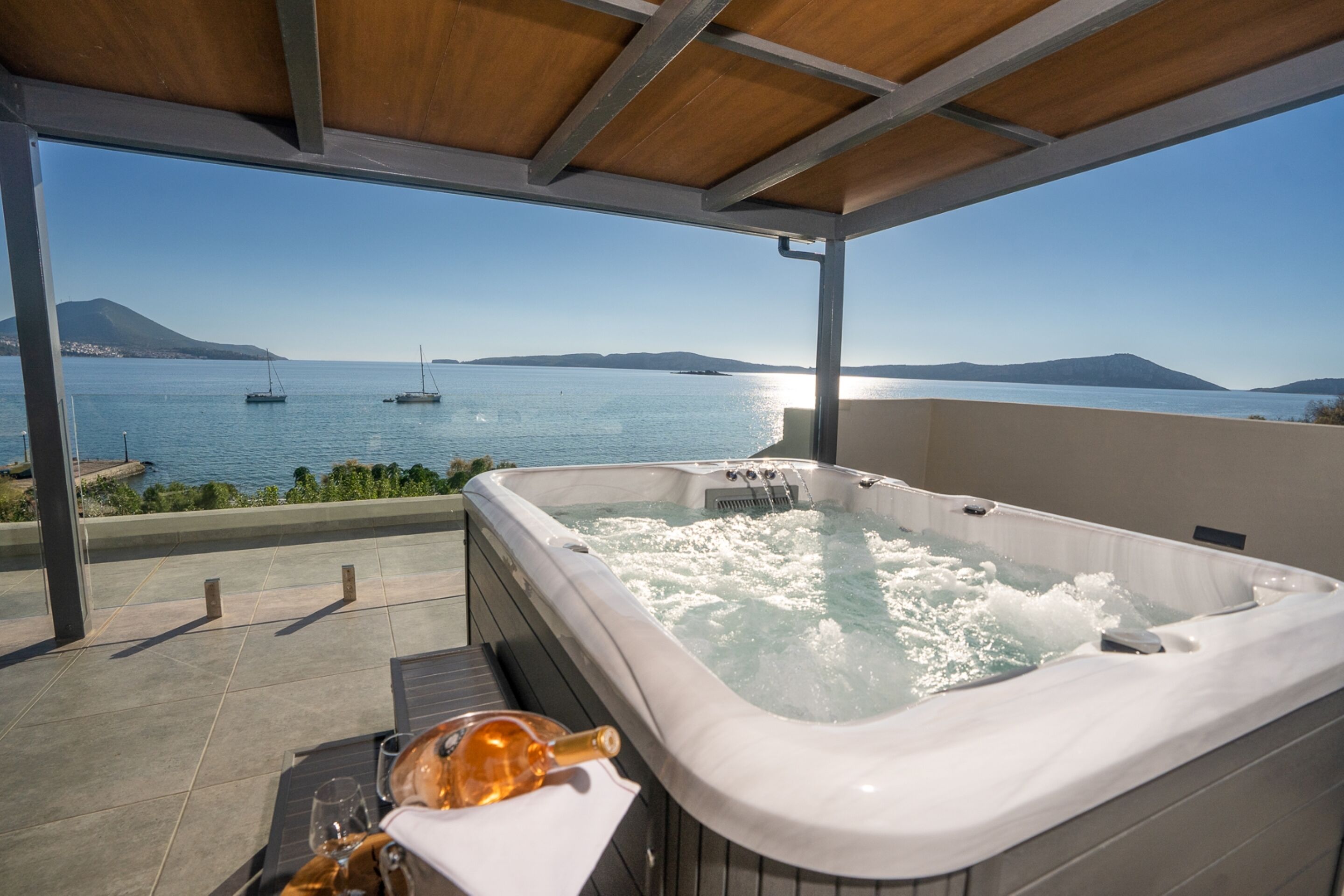 Un bain à remous avec vue sur la mer et les bateaux, une bouteille de champagne et un verre posé sur une table.