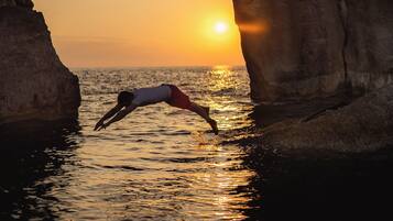 Una persona se sumerge en el agua al atardecer a través de un arco de roca.
