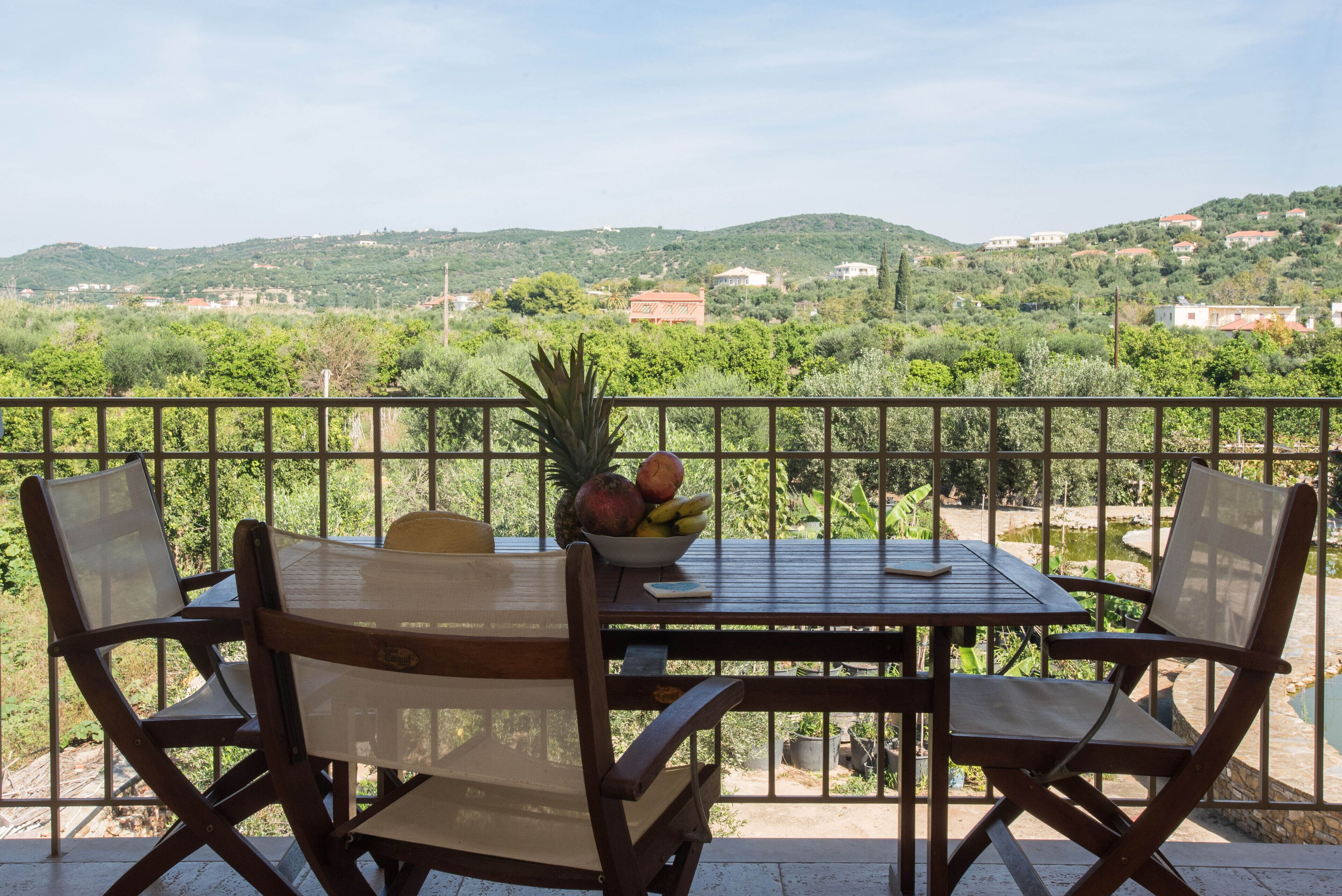 A balcony with a table set for two, chairs, and a bowl of fruit.