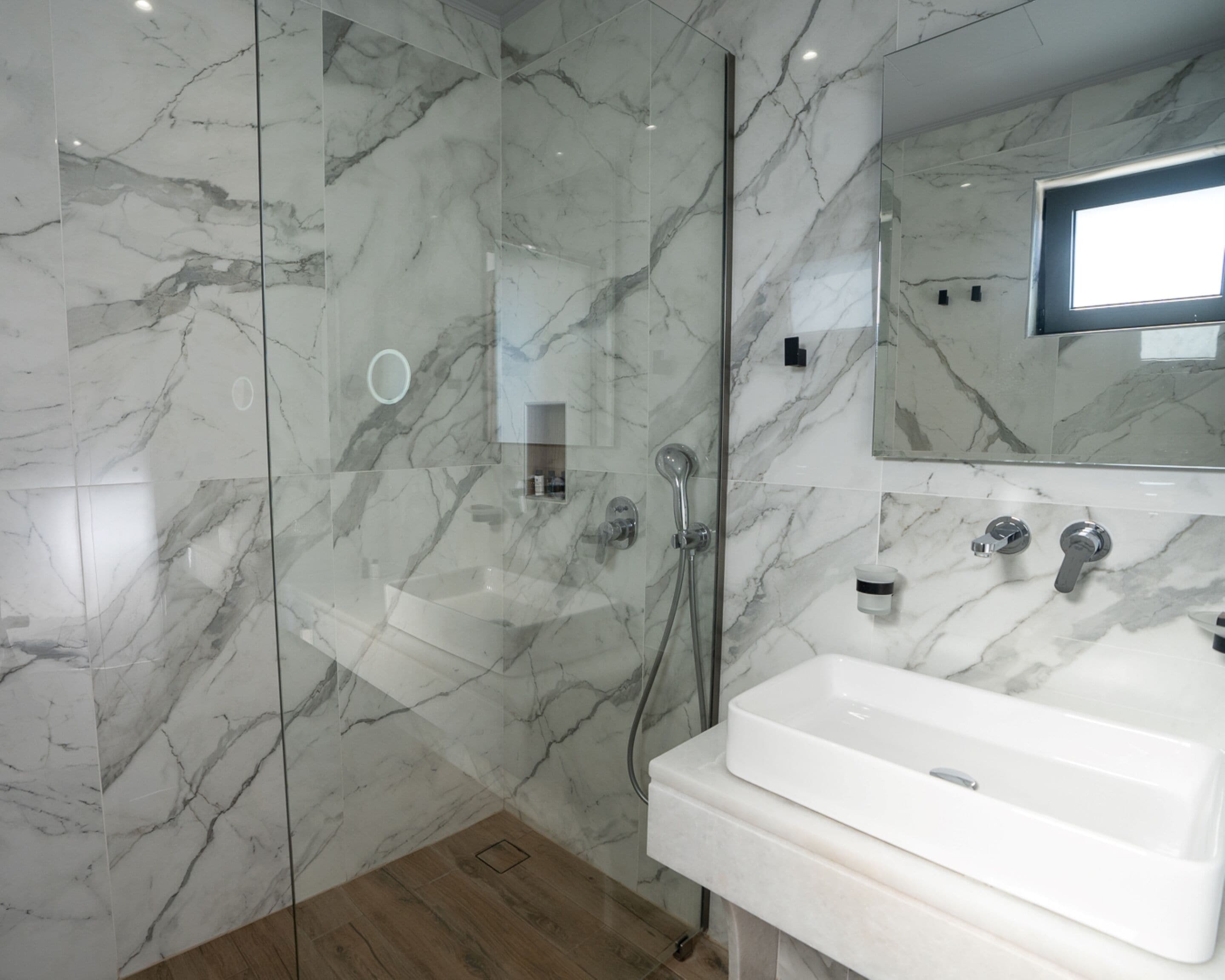 Une salle de bain moderne avec une douche à parois de verre, un lavabo blanc et un pare-baignoire en marbre.