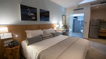 A modern hotel room with a large bed, bedside lamps, a wooden nightstand, a mirror, and a view of the bathroom and kitchen.