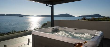 A hot tub on a balcony with a view of the sea and hills.
