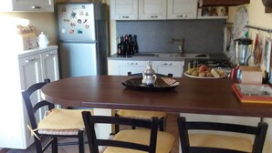 Une cuisine équipée d’une table à manger, de chaises, de placards, d’un réfrigérateur et de divers ustensiles de cuisine.