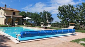 Un espace piscine avec des chaises longues et des parasols, une maison avec un toit en tuiles et un ciel dégagé.