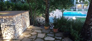 Paredes de pedra, plantas em vasos e uma piscina com espreguiçadeiras.