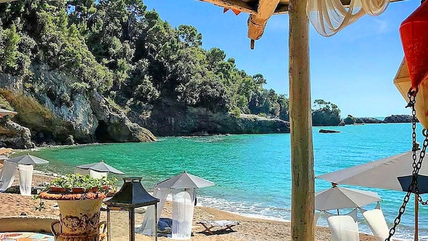 Een strand met helder turquoise water, houten pergola's en parasols.