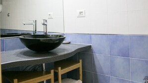 A bathroom with a black vessel sink, a white pedestal sink, and a mirror above the sink. There are shelves with towels and a small trash bin. - Casa Niccolo apartment complex (Napoli)