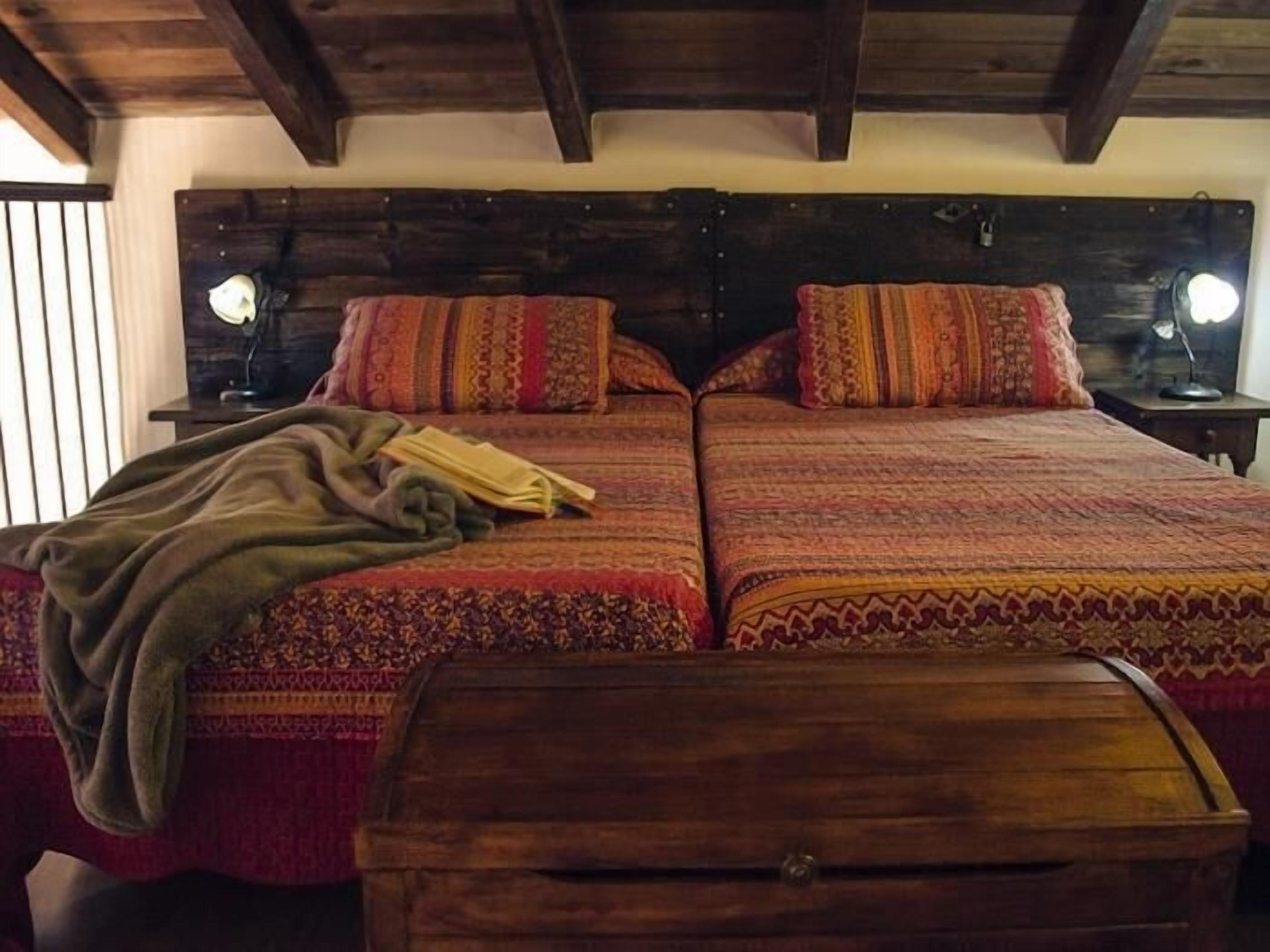Un lit double avec une literie à motifs, deux tables de chevet avec des lampes et une commode en bois au premier plan.