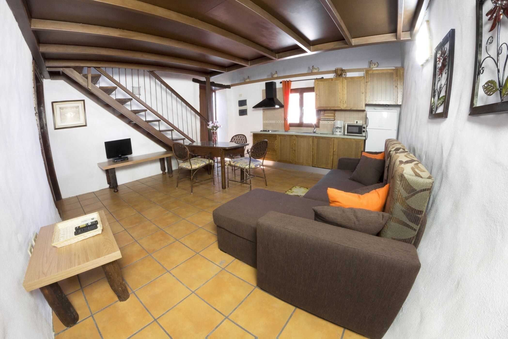 A living room with a sofa, a small table, a TV, and a staircase leading to a kitchen.