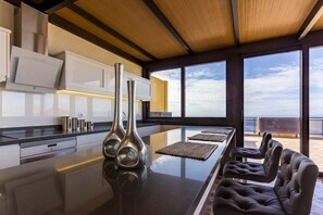 A modern kitchen with a long island, two stainless steel vases, and a seating area with leather chairs. - Gran Villa Vilena (Tijoco Bajo Adeje)