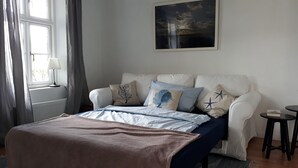 Un dormitorio con cama, mesita de noche, lámpara y ventana con cortinas.