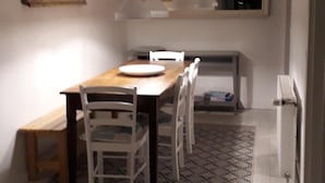 Un comedor moderno con una mesa de madera y sillas blancas, una alfombra estampada e iluminación colgante.