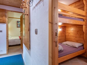 Une chambre avec un lit superposé en bois et une porte donnant sur une autre pièce.