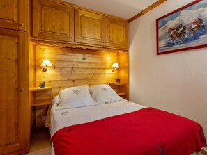 A wooden cabin-style bedroom with a bed, two bedside lamps, and a painting on the wall.