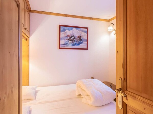 A hotel room with a bed, a painting of a snowy mountain scene, and a wooden door.