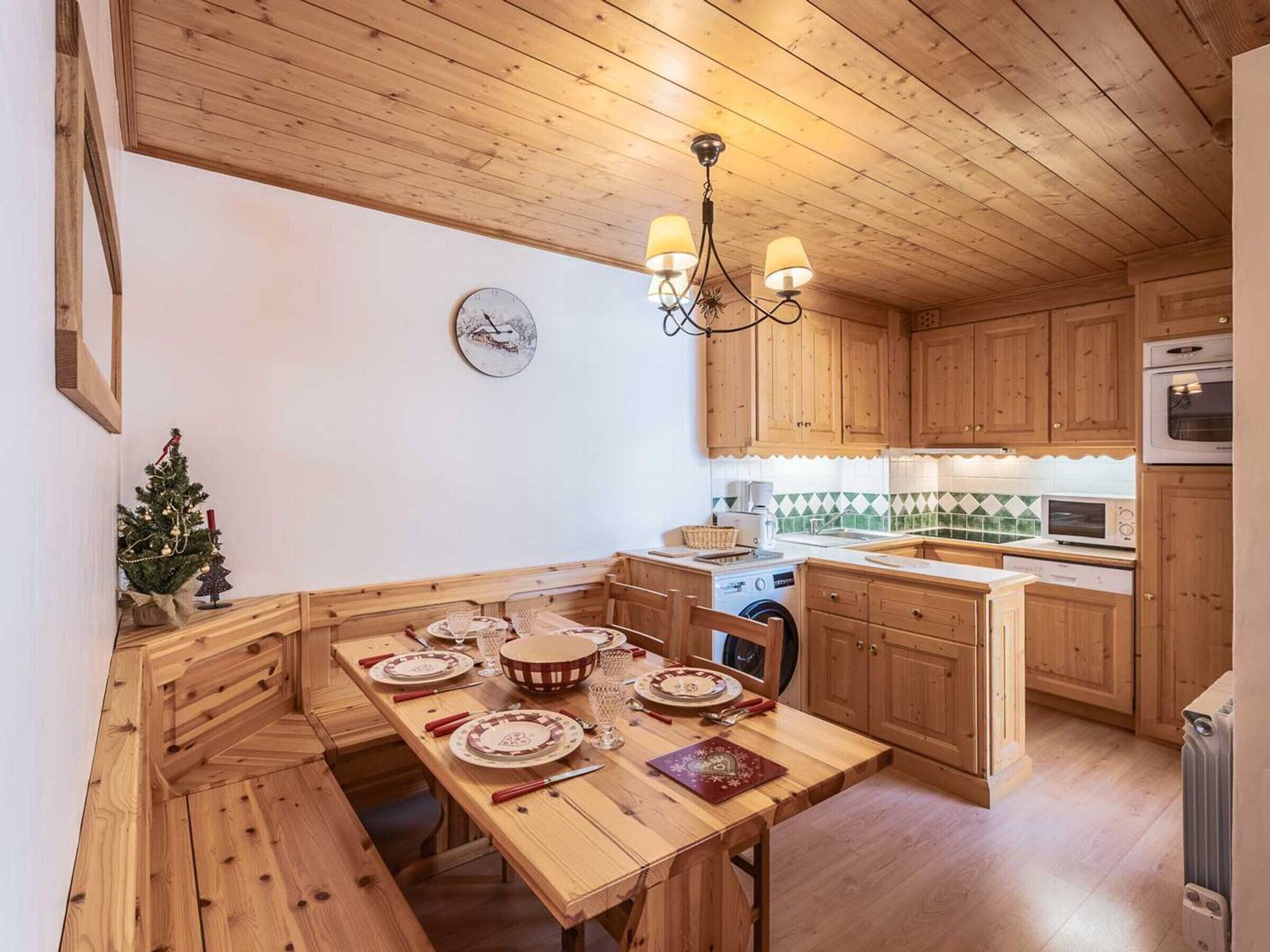 Un interior de madera con una mesa de comedor preparada para cuatro, una cocina con armarios de madera y un pequeño árbol de Navidad.