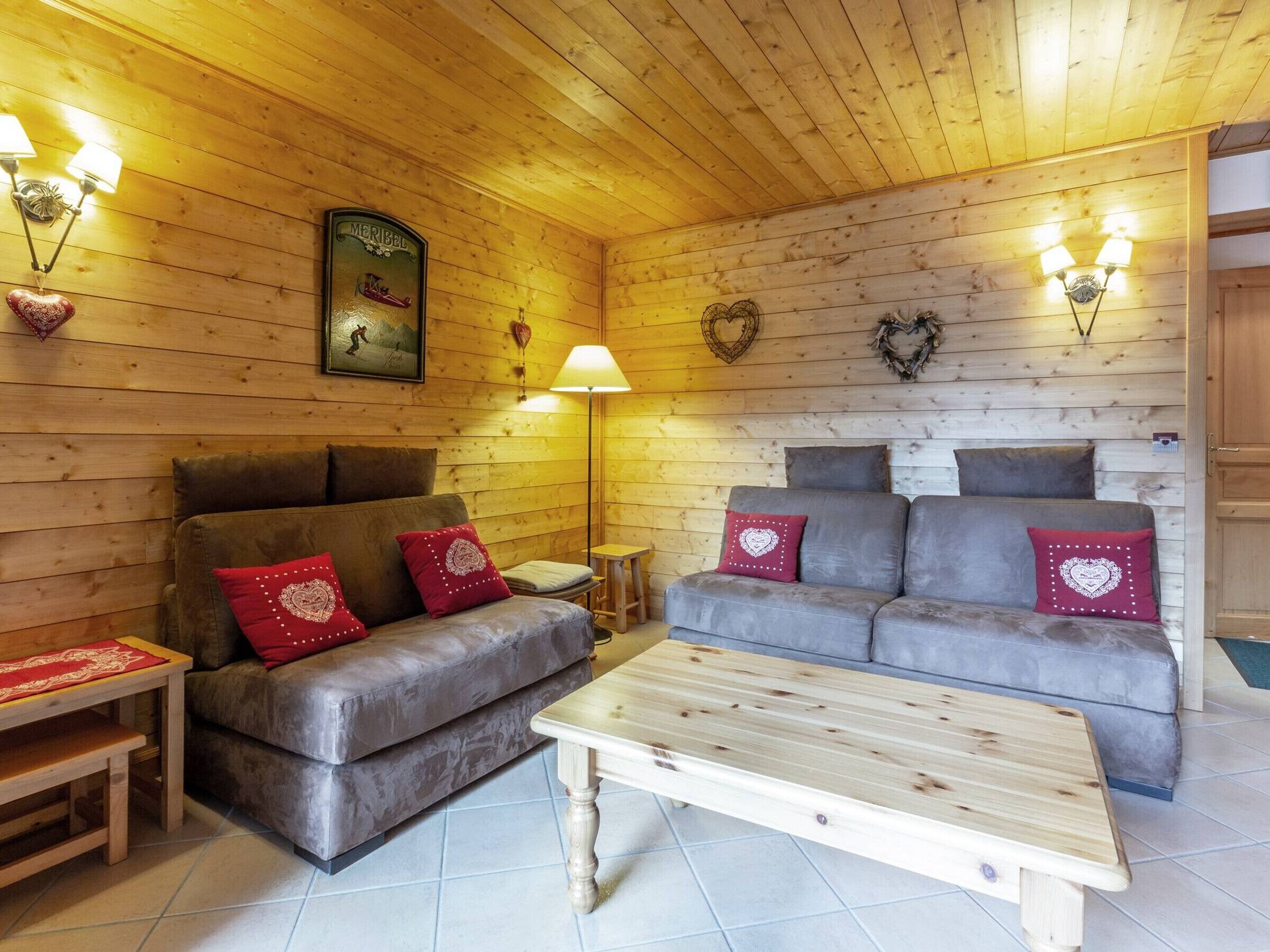 A cozy room with a wooden ceiling, a sofa set, a small table, and wall-mounted lamps.
