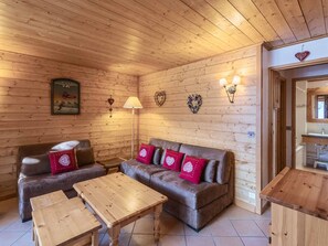 A cozy room with wooden walls, a sofa with red cushions, a wooden table, and a lamp.