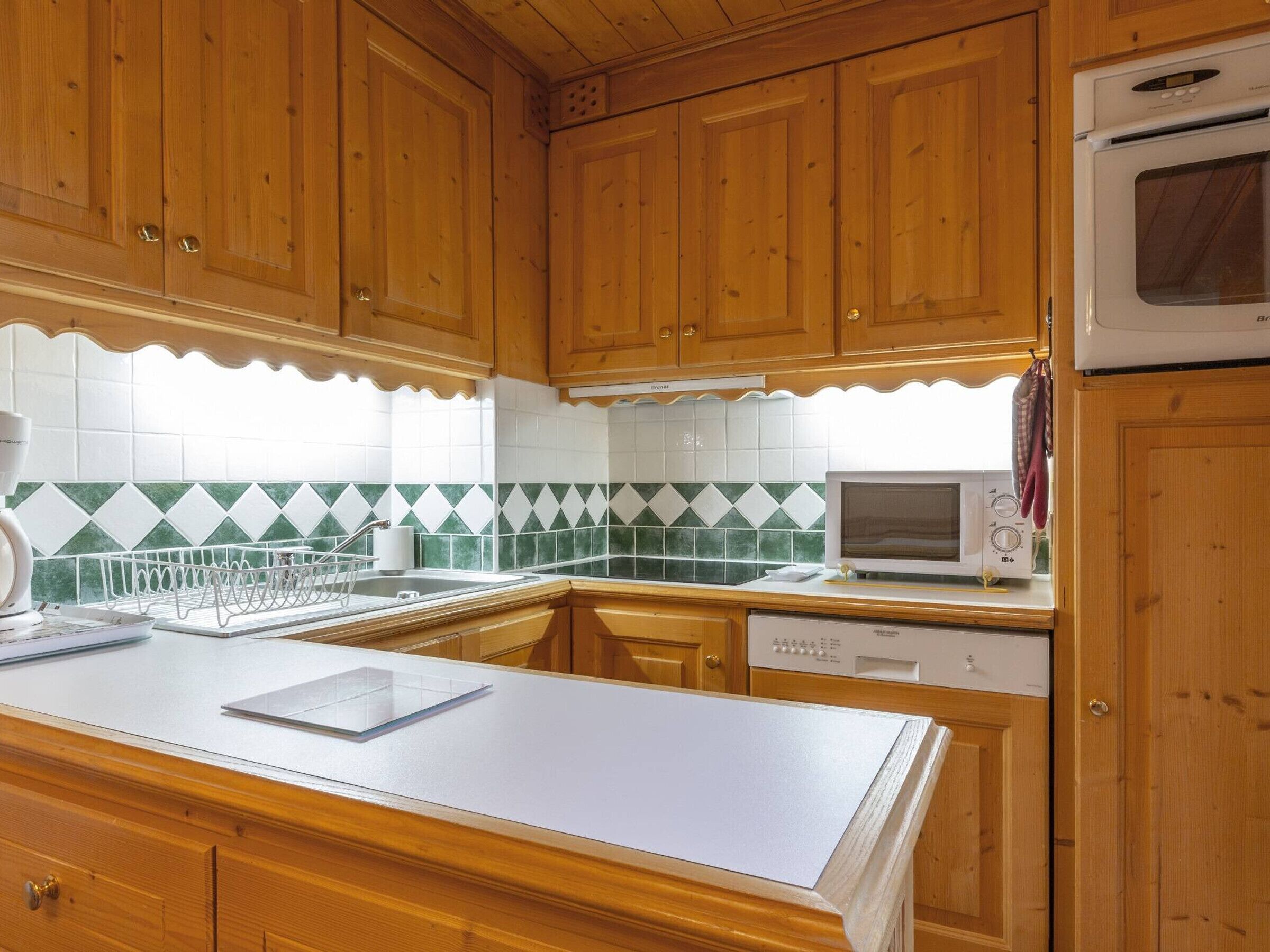A kitchen with wooden cabinets, a white countertop, a microwave, and a dishwasher.