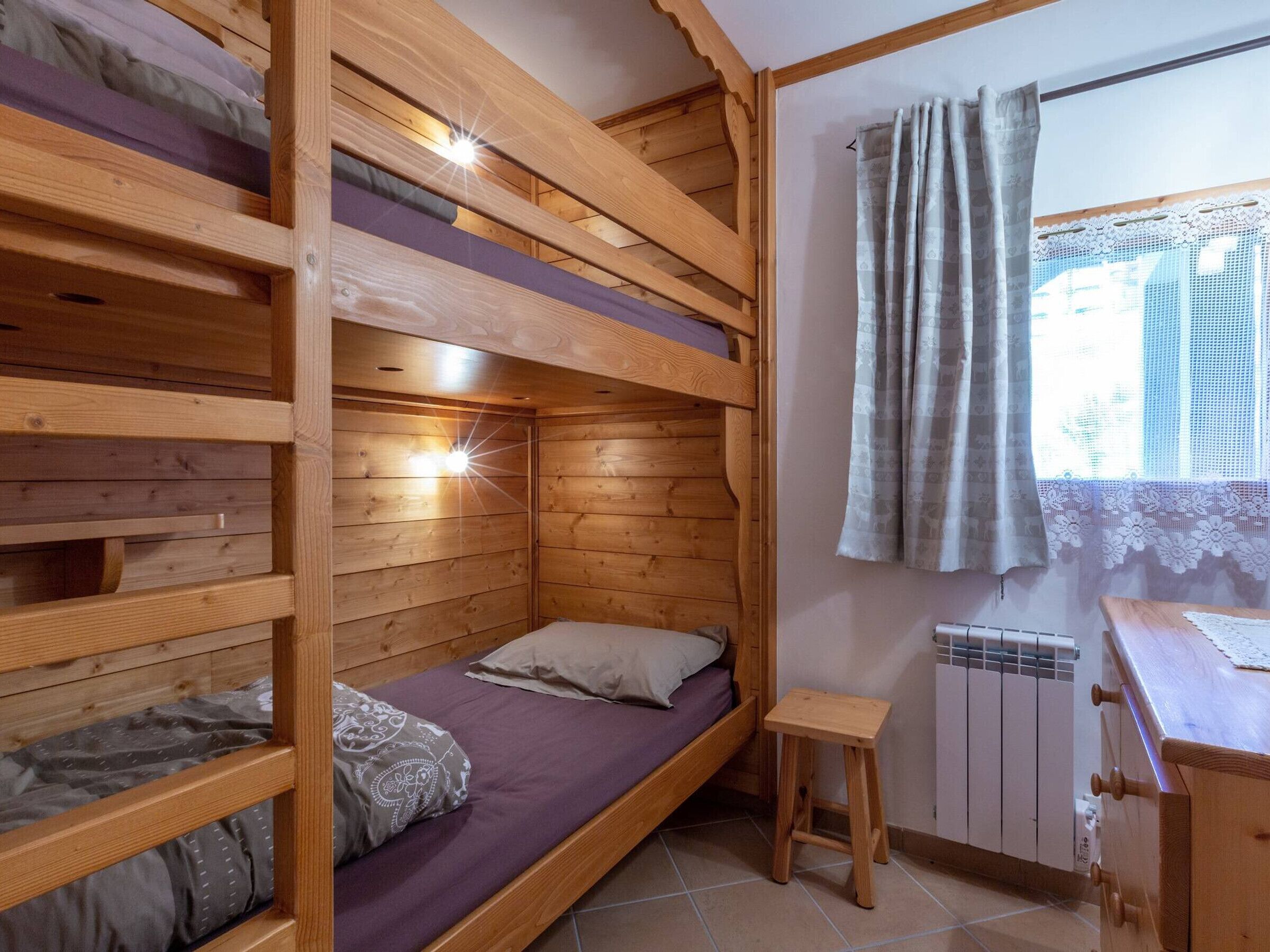 A bunk bed room with a small stool and a radiator.