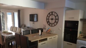 Une cuisine compacte avec un coin repas, une grande horloge murale, un lave-linge et un téléviseur fixé au mur.