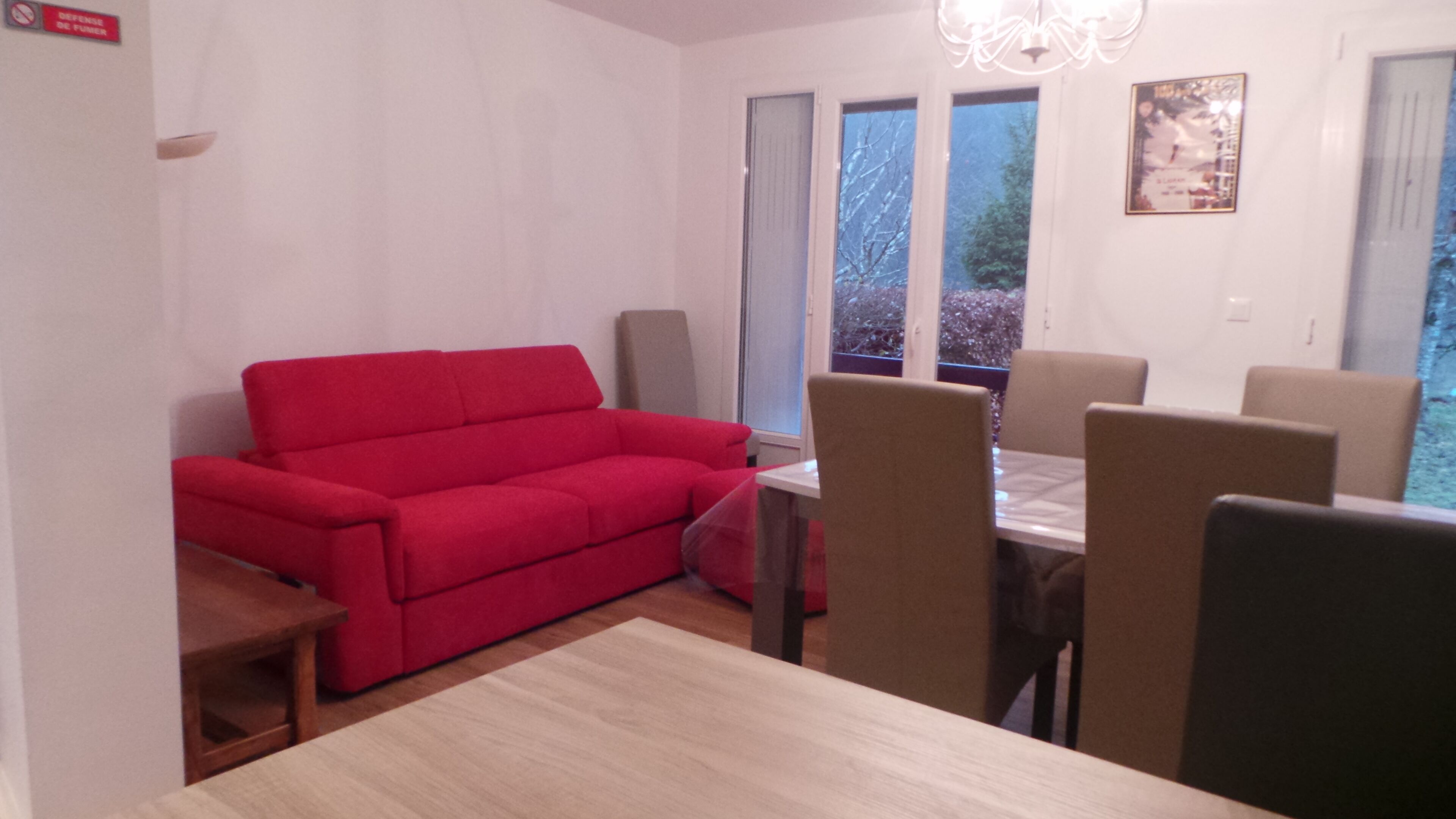 A room with a red sofa, a dining table with chairs, and a chandelier.