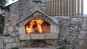 Ein Kamin aus Stein im Freien mit Feuer, umgeben von Holzscheiten und einem Holzzaun.