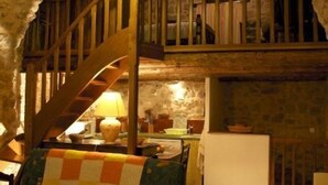 Ein rustikaler Raum mit einer Holztreppe, einem Tisch mit Lampe und einem gesteppten Sessel.