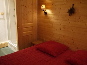 Quarto com painéis de madeira, uma cama, uma mesa de cabeceira e uma luminária fixada na parede.
