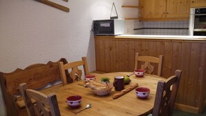 A wooden dining table with six chairs, a microwave, and a small potted plant on the counter.