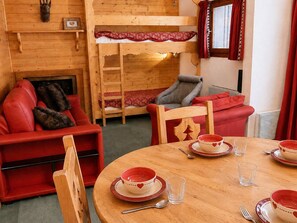 Um quarto aconchegante com uma cama beliche, um sofá vermelho, uma mesa de jantar posta com pratos e tigelas, e uma lareira.