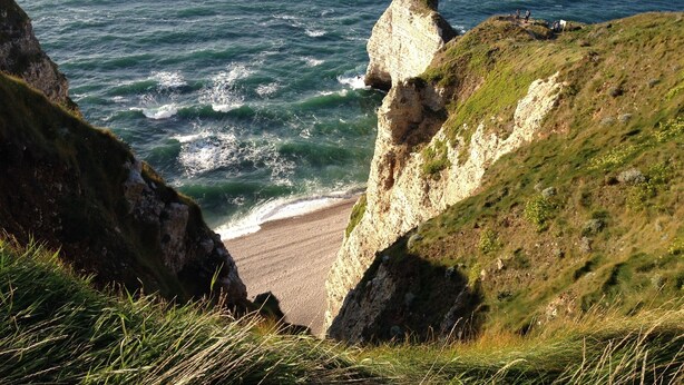A coastal landscape with a prominent cliff, a beach, and the ocean.