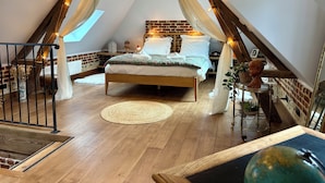 A cozy, triangular loft bedroom with a bed, a small table, and a hanging light fixture labeled "HOTEL".