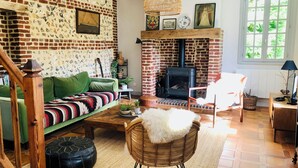A cozy living room with a brick fireplace, green sofa, wicker chair, and a wooden coffee table.