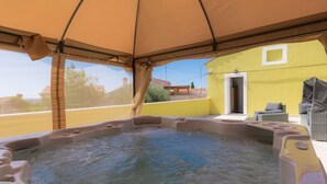 Ein Whirlpoolbereich mit Baldachin, ein gelbes Gebäude und Gartenmöbel.
