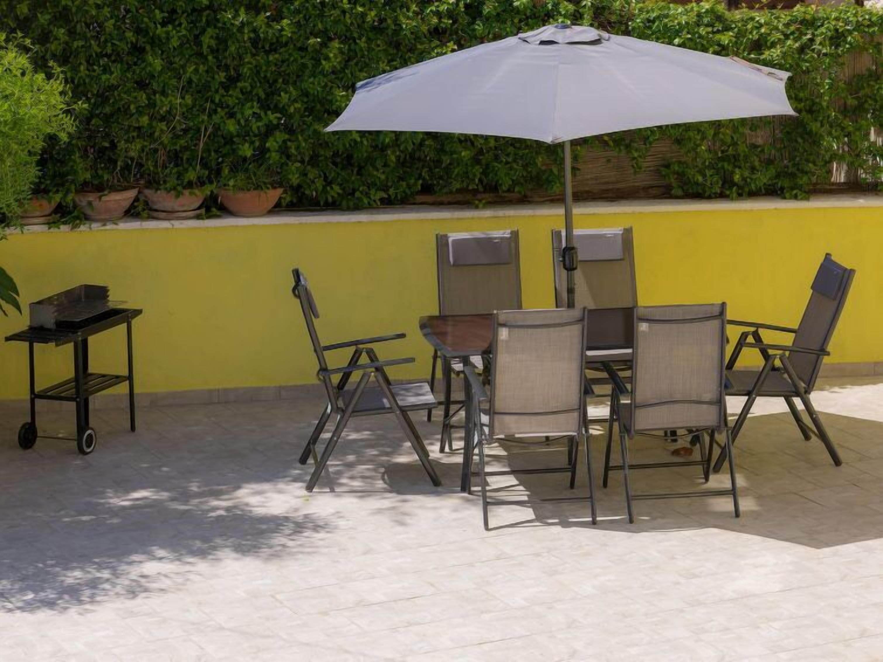 Une terrasse extérieure avec une table et des chaises, un chariot et un grand parasol.