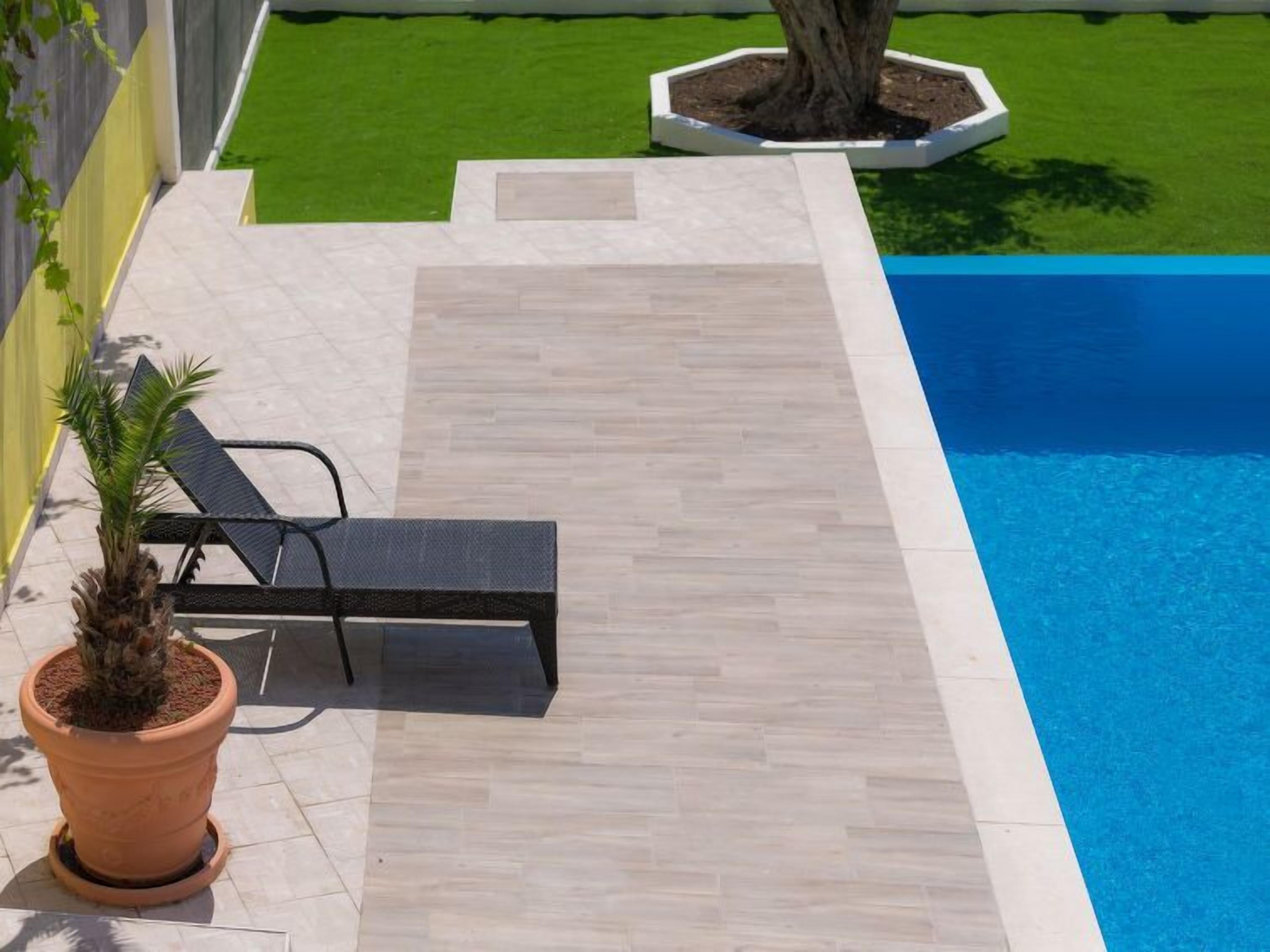 Un espace aménagé au bord de la piscine, comprenant une chaise longue, un pot de fleurs et un grand bac pour arbre.