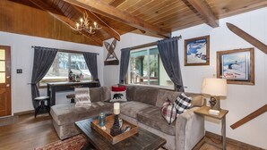 Un salon chaleureux avec un plafond en bois, un ensemble de canapés, une table basse et un coin repas avec vue sur l’extérieur par une fenêtre.