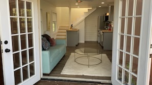 A modern interior with a light blue sofa, a glass coffee table, and a staircase leading to a kitchen area.