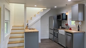 A modern kitchen with grey cabinets, stainless steel appliances, and a wooden staircase.