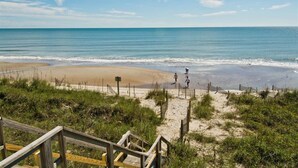 Een strand met een houten looppad dat naar het strand leidt, omringd door begroeiing.