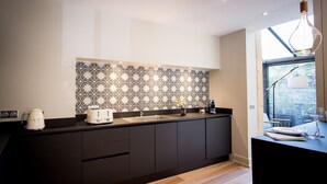 A modern kitchen with dark cabinetry, a patterned backsplash, and a window providing natural light. - Elisabeth's suite in the heart of the medieval center of Sarlat (Sarlat-la-Canéda)
