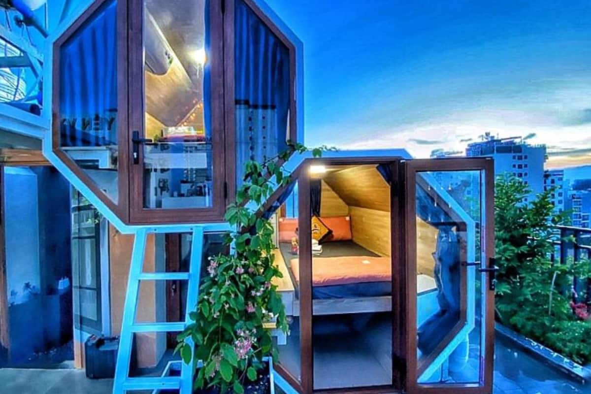 A modern, multi-level octagonal structure with a glass exterior, a visible staircase, and a bed with a pillow.