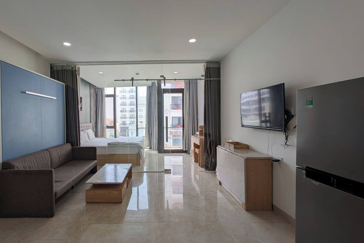 A modern hotel room with a sofa, a small table, a TV, and a refrigerator.