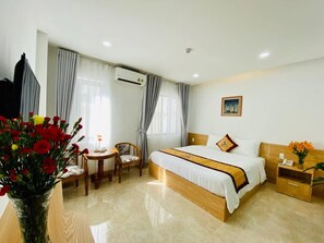 A hotel room with a bed, bedside table, chair, and a desk with a vase of red flowers. - Blue S Hotel & Apartment (Da Nang)
