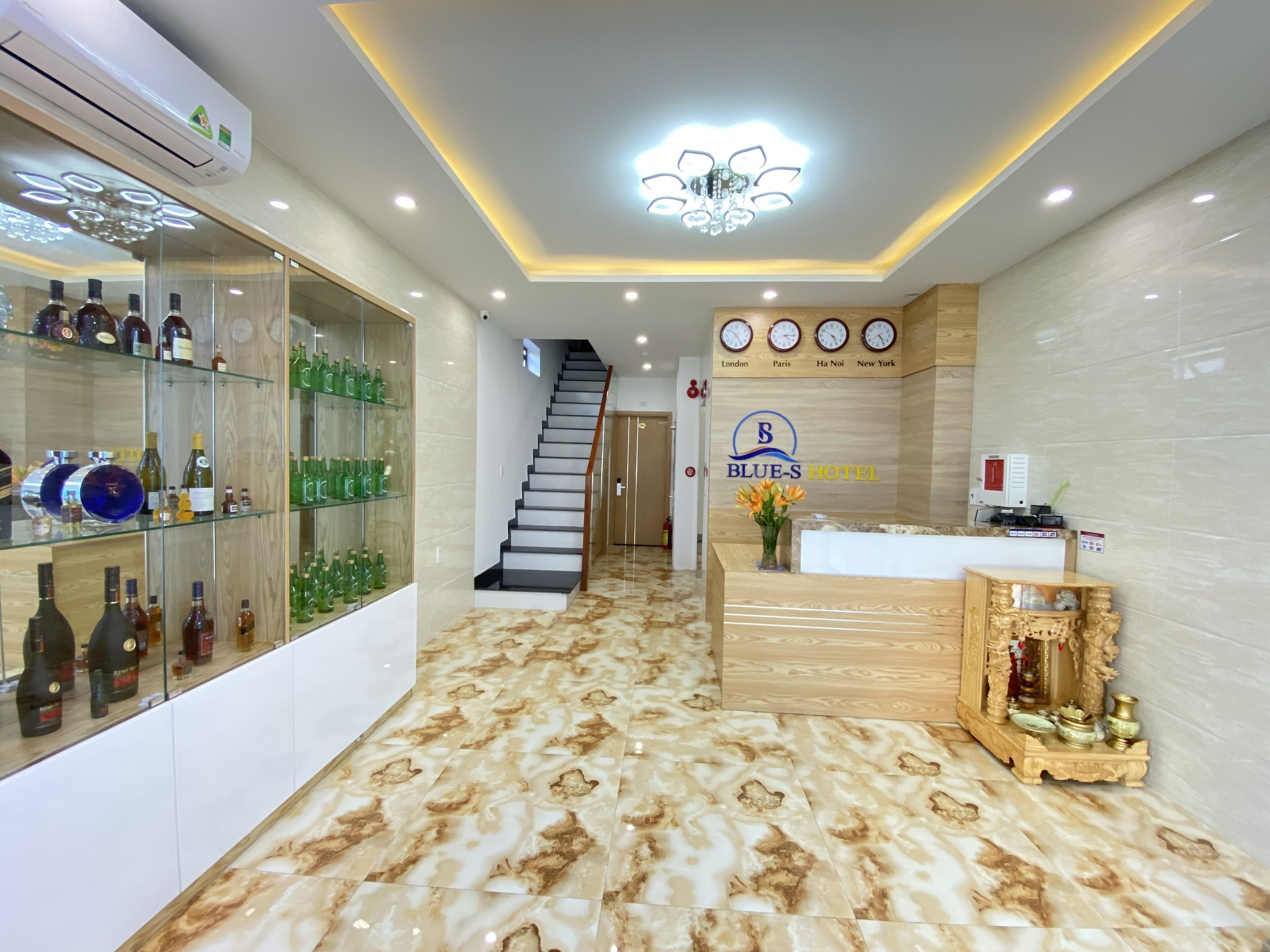 A hotel reception area with a marble floor, a staircase, and a display of liquor bottles.