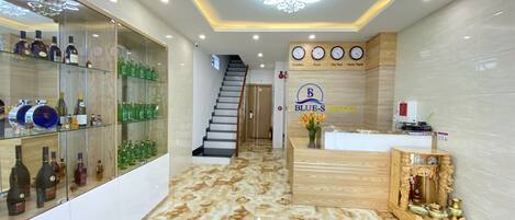 A hotel reception area with a marble floor, a staircase, and a display of liquor bottles.