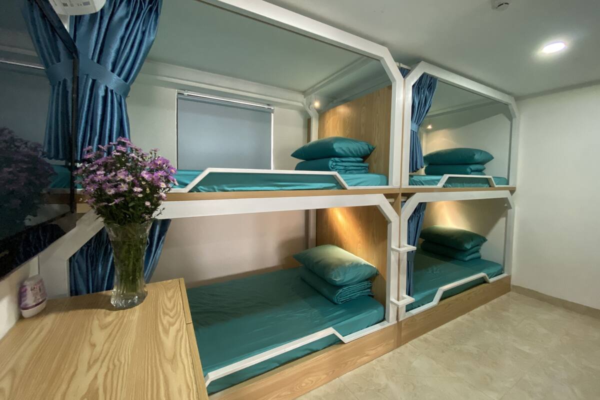 A bunk bed room with a wooden headboard, teal bedding, and a vase of flowers on a wooden table.